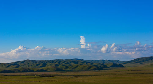 Scenic view of field and mountains against blue sky