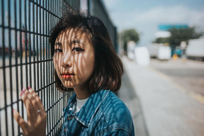 Close-up portrait of young woman by fence