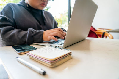 Midsection of man using mobile phone while sitting on table at home