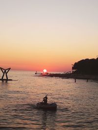 Silhouette people in sea against clear sky during sunset