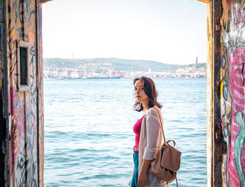 Portrait of woman standing by river in city against sky