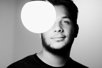Close-up portrait of young man with illuminated light bulb at home