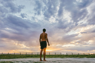 Young man standing in bathing suit against sunset in meadow hot spring