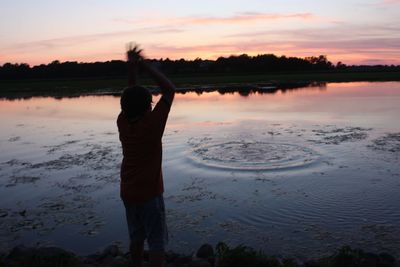 Rear view of man looking at lake during sunset