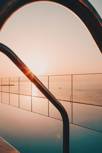 Railing by sea against clear sky during sunset