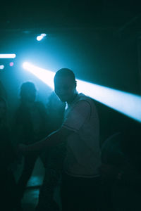 Young man dancing against illuminated spotlight at nightclub