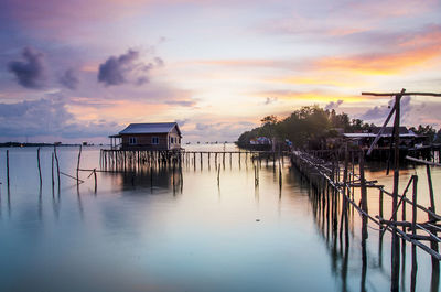 Stilt house in river against cloudy sky during sunset