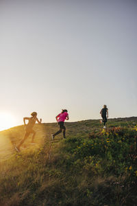 Women running up on hill during group training session against sky