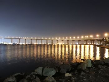 Illuminated bridge over sea against sky at night