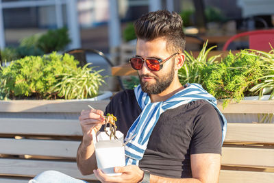 Young man wearing sunglasses sitting on plant