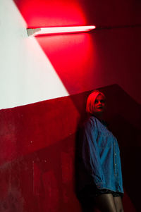 Low angle view of young woman looking away while standing against wall