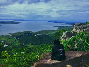 Rear view of people sitting on rock by sea against sky