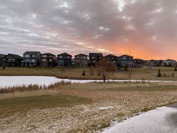 Houses on field by buildings against sky during sunset