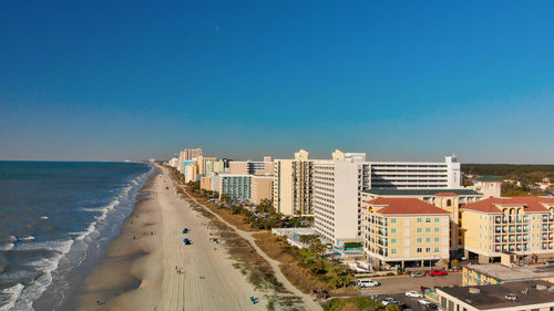 Panoramic view of beach and buildings against clear blue sky