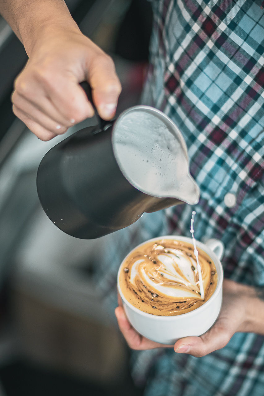 CROPPED IMAGE OF HAND POURING COFFEE CUP