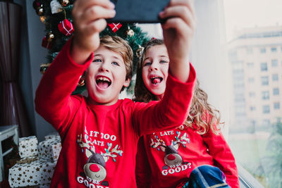 Brother and sister at home taking a selfie with mobile phone.kids sitting by christmas tree
