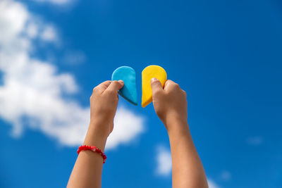 Cropped hand of woman holding heart shape against blue sky