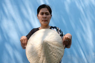 Mature woman holding asian style conical hat against wall