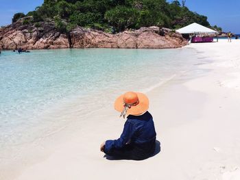 Rear view of man sitting on beach against sky