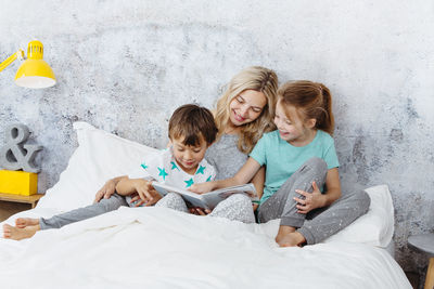 Mother and children reading book on bed at home