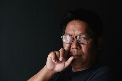 Portrait of mature man wearing eyeglasses against black background