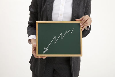 Midsection of businesswoman showing diagram on blackboard while standing against white background