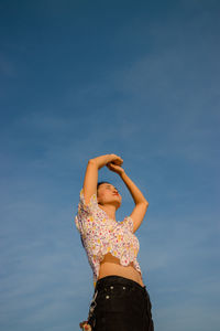 Low angle view of woman standing against blue sky