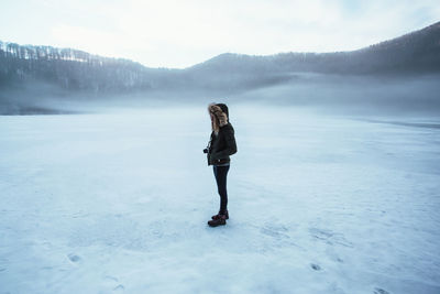 Side view of woman standing on frozen lake against sky