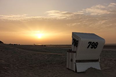 Hooded chairs on beach against sky during sunset