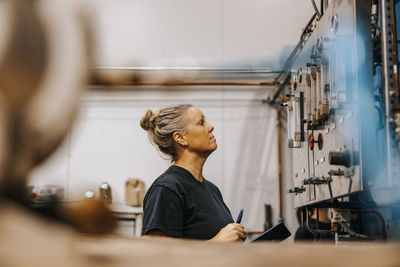 Side view of mature female worker examining circuit in metal factory