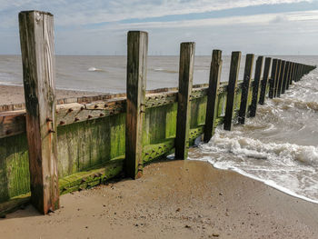 Wooden posts on beach against sky