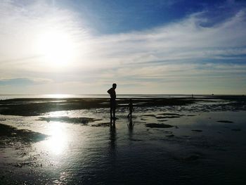 Silhouette boy standing on beach against sky during sunset