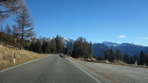 Road amidst trees against clear blue sky