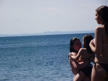 Mother carrying daughter by friend at beach during summer