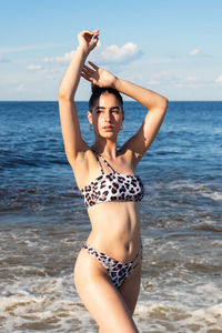 Full length of young woman standing at beach against sky