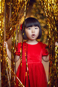 Portrait of a beautiful korean baby girl in a red dress at christmas with a gold decoration