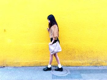 Full length of woman standing on footpath against yellow wall