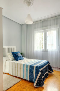 Interior of cozy single bedroom decorated with quilt and curtains