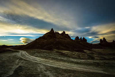 Desert dirt road in front of natural rock formations of trona pinnacles and cloudy sky