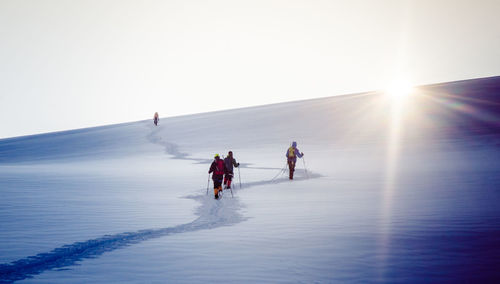 People skiing on mountain against clear sky during winter 