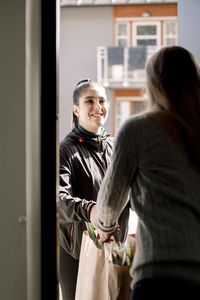 Young delivery woman delivering grocery to female customer at home