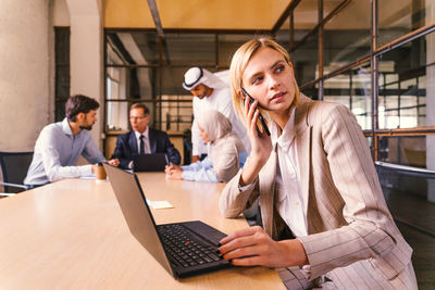 Young woman using laptop while standing in office