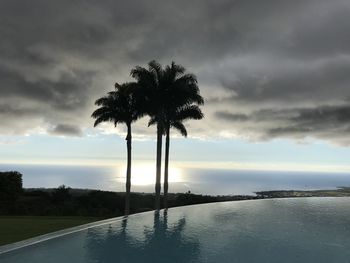 Palm trees by swimming pool against sky during sunset