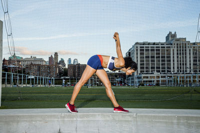 Female athlete exercising while standing on retaining wall by net during sunset