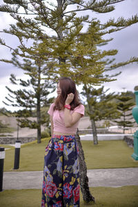 Young woman standing against tree at park