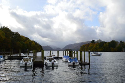 Boats moored in lake against cloudy sky