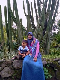 Portrait of mother and son sitting against cactus 