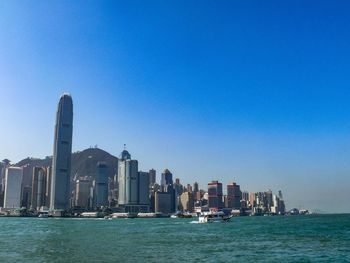 Sea by modern buildings against clear blue sky