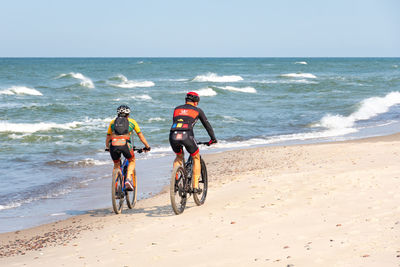 People riding at beach against sky