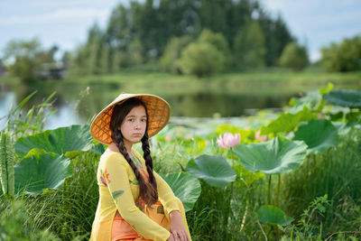 Woman wearing straw hat standing near the lotuses lake
